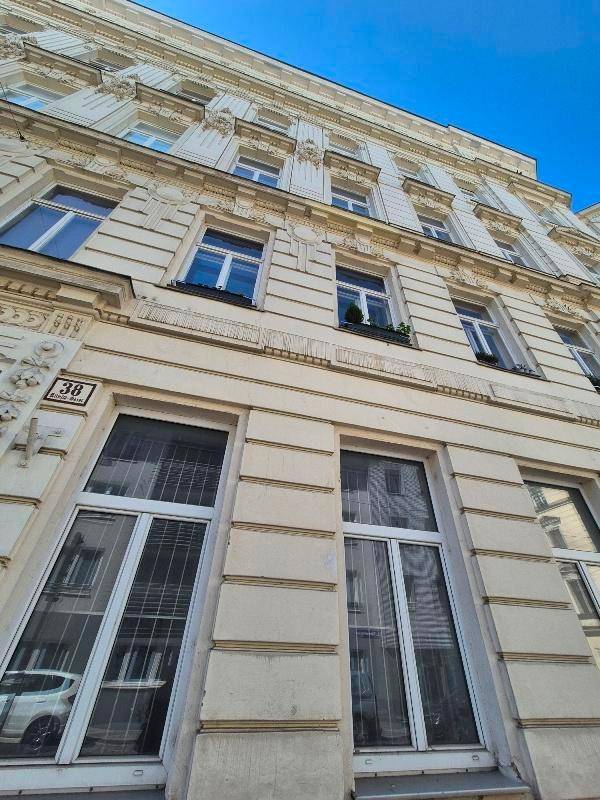Historische Fassade eines Altbaus mit reich verzierten Details und großen Fenstern.