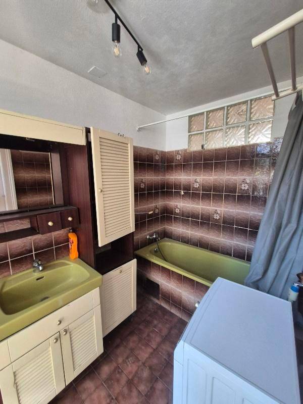 Badezimmer mit olivgrüner Badewanne und Waschbecken, braunen Fliesen und Glasbausteinfenster.