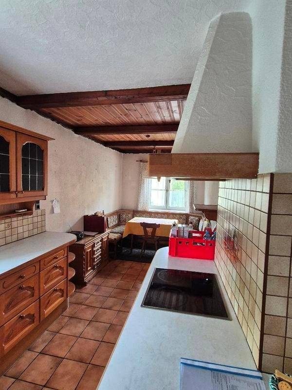Gemütliche Küche mit Holzbalkendecke, gefliestem Boden und einer Essecke am Fenster.