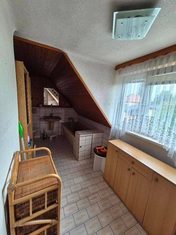Badezimmer im Dachgeschoss mit schräger Decke, Fliesenboden und Fenster.