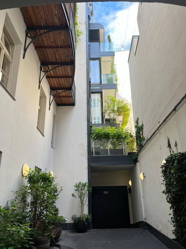Schmaler Innenhof mit moderner und traditioneller Architektur, begrünten Balkonen und Garagenzugang.