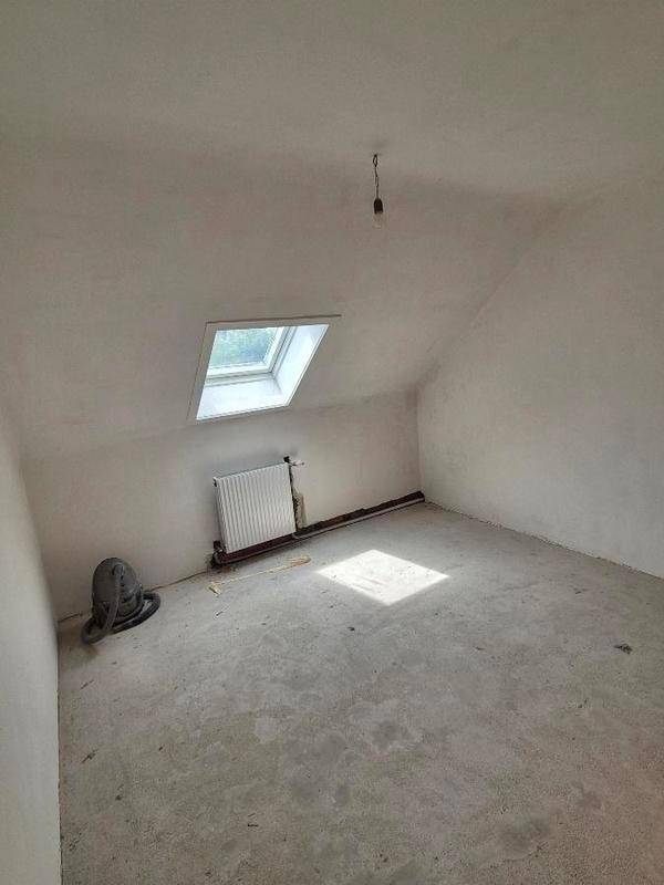 Dachgeschossraum mit schrägen Wänden, Dachfenster und Betonboden, bereit für den Ausbau.