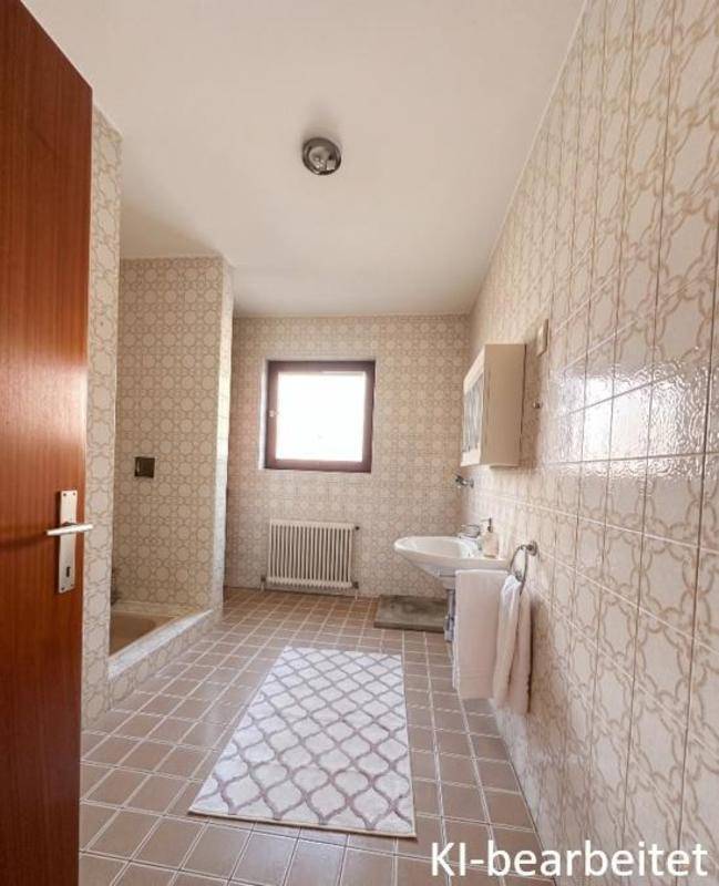 Badezimmer im Stil der 80er Jahre mit gemusterten Fliesen, Badewanne und Fenster.