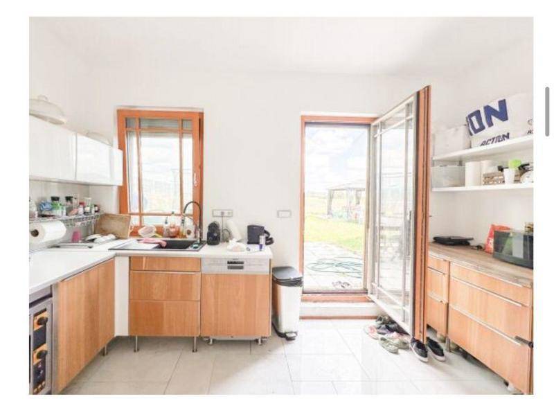 Funktionale Küche mit Holzschränken, weißen Arbeitsplatten und direktem Gartenzugang.
