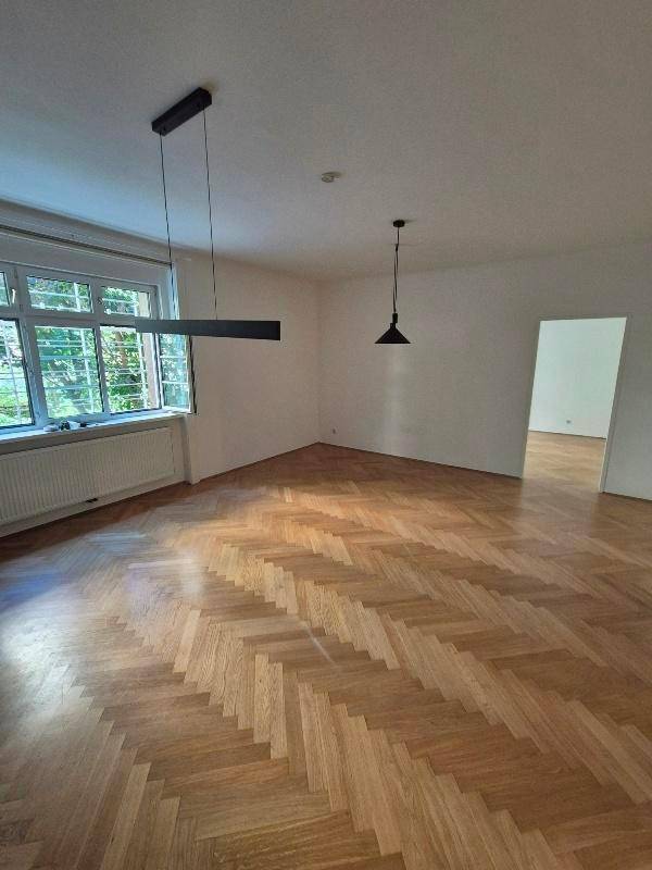 Heller, leerer Wohnraum mit Fischgrätparkett und großen Fenstern, bereit zur individuellen Gestaltung.