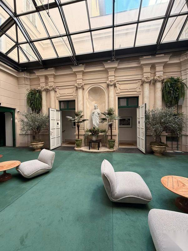 Überdachter Innenhof mit Glasdach, Sitzgelegenheiten und klassischer Architektur mit Statuen.