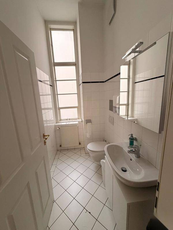 Helles Badezimmer mit weißen Fliesen, Fenster und modernem Waschtisch.
