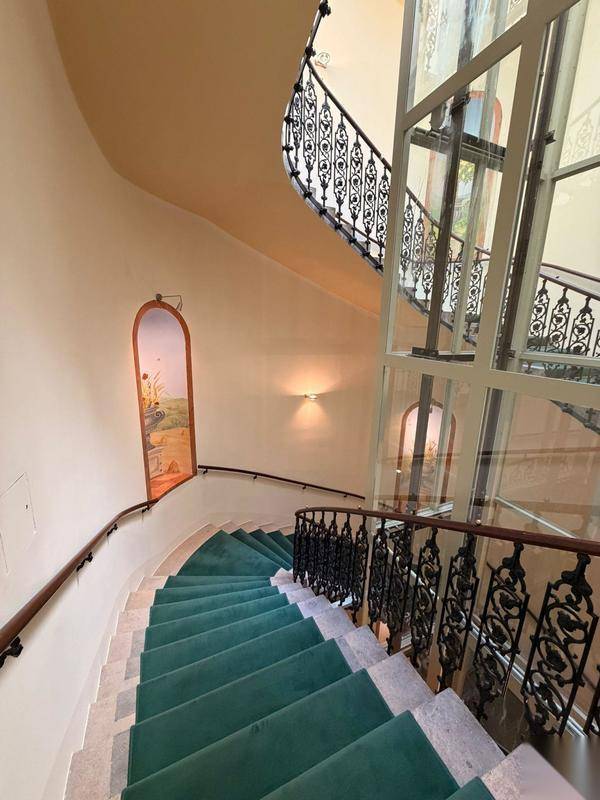 Elegantes Treppenhaus mit Teppichläufer, schmiedeeisernem Geländer und modernem Glasaufzug.