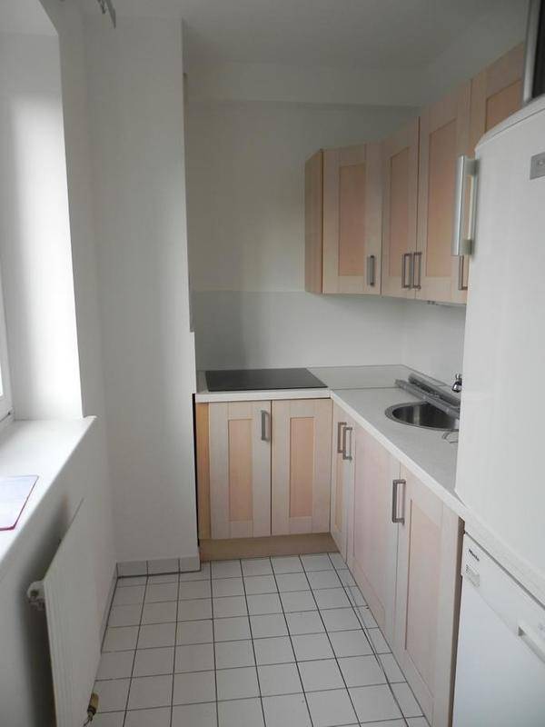 Funktionale Küche mit hellen Holzschränken, weißer Arbeitsplatte, Induktionskochfeld und Fliesenboden.
