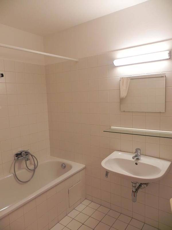 Helles Badezimmer mit weißen Fliesen, Badewanne mit Duschfunktion und einem Waschbecken mit Spiegelschrank.