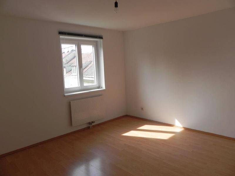 Helles Schlafzimmer mit Holzboden, weißen Wänden und einem Fenster, das viel Sonnenlicht hereinlässt.