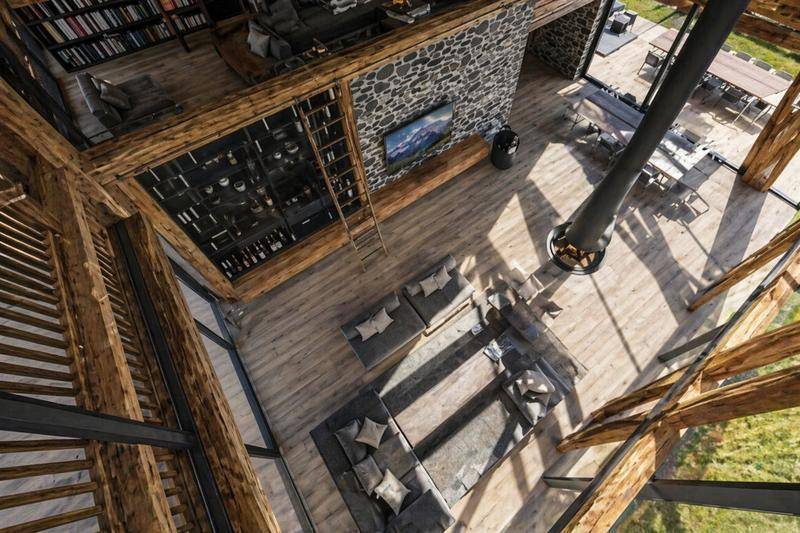 Offener Wohnbereich mit hohen Decken, Steinwand, Bibliothek auf der Empore und freistehendem Kamin.