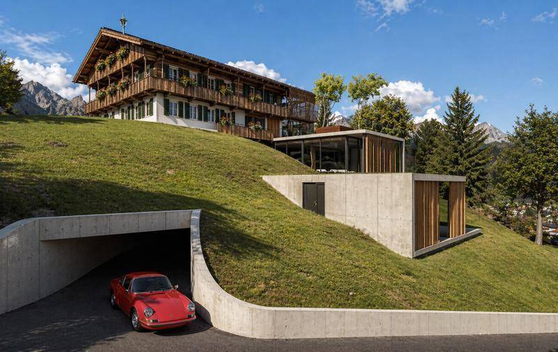Gesamtanlage des Alpenhauses mit moderner Erweiterung, Tiefgaragenzufahrt und Bergblick auf einem Hügel.