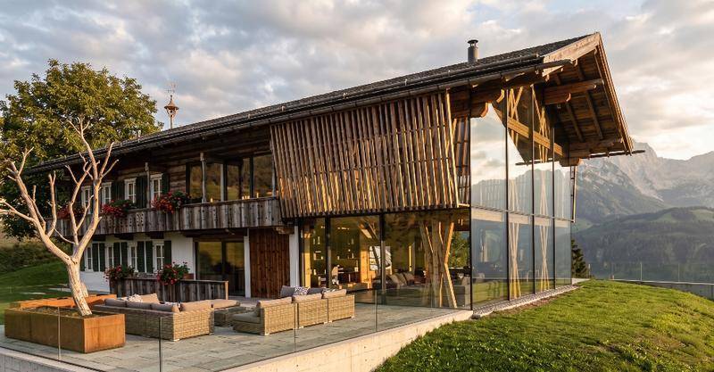 Moderne Villa im Chalet-Stil mit Glasfassade, Holzverkleidung und einer möblierten Terrasse mit Bergblick.