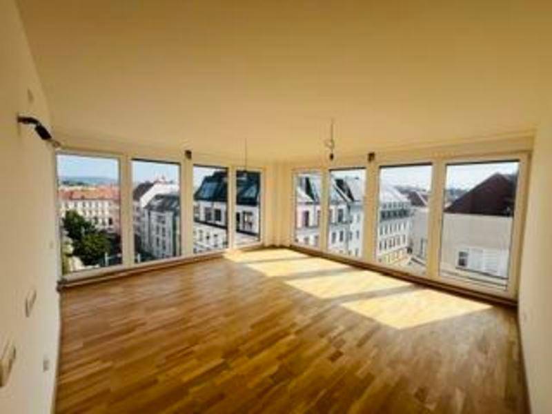 Heller Wohnraum mit großen Fenstern, Parkettboden und weitem Blick über die Stadt.