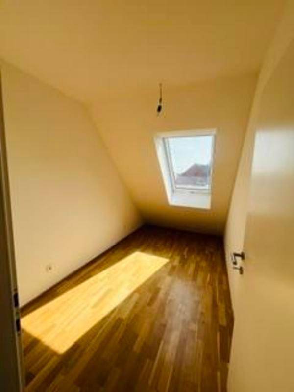 Helles Dachzimmer mit schrägen Wänden, Holzboden und einem Dachfenster.