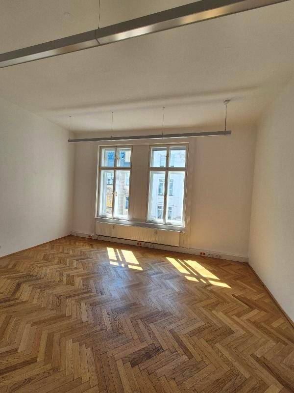 Heller Raum mit Fischgrätparkett, großen Fenstern und viel natürlichem Licht.