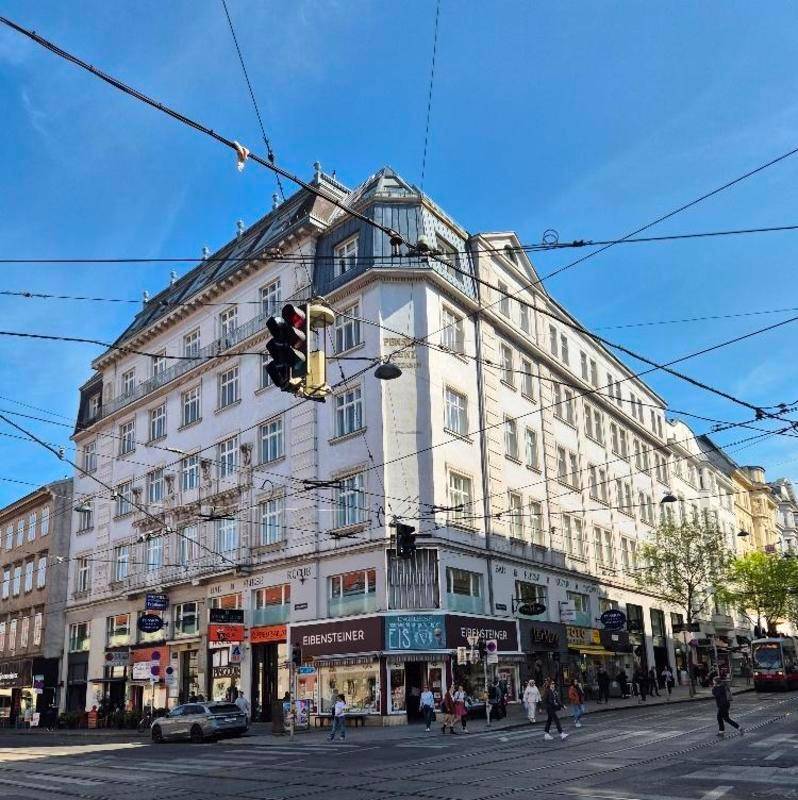Historisches Eckgebäude mit vielen Fenstern und Geschäften im Erdgeschoss an einer belebten Straße.