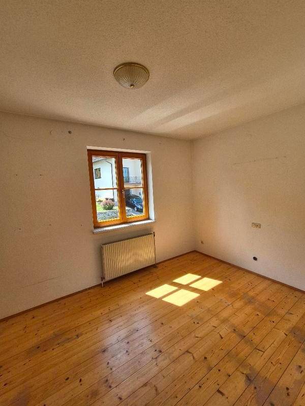 Helles Zimmer mit Holzdielenboden, Fenster und Heizkörper.