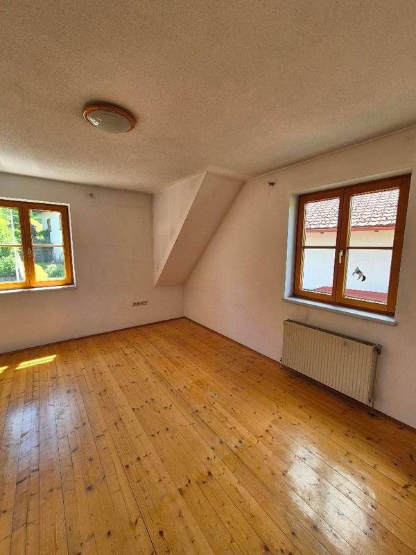 Helles Schlafzimmer mit Holzdielenboden, Heizkörper und Fenstern mit Ausblick.