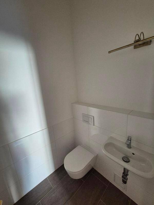 Kompaktes Gäste-WC mit Wand-WC, kleinem Waschbecken und modernen Fliesen an Wand und Boden.