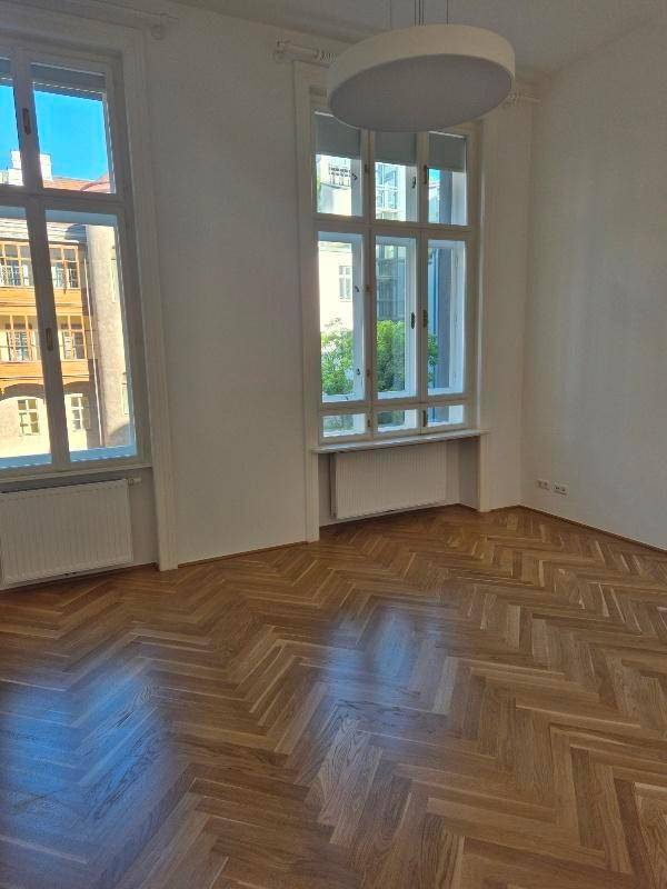 Helles Zimmer mit Fischgrätparkett, hohen Fenstern und moderner Deckenleuchte, ideal für Wohnzwecke.