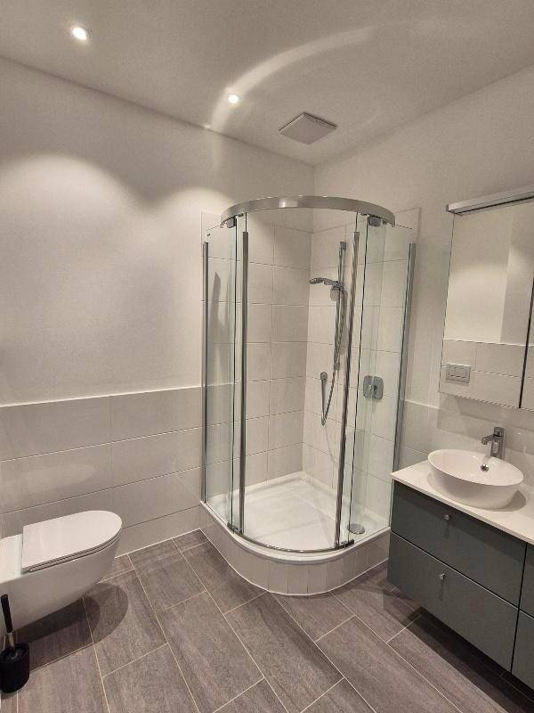 Modernes Badezimmer mit Eckdusche, Waschtisch und wandhängendem WC, ausgestattet mit grauen Fliesen.