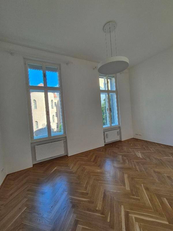 Helles Zimmer mit Fischgrätparkett, hohen Fenstern und moderner Deckenleuchte, bietet viel Tageslicht.