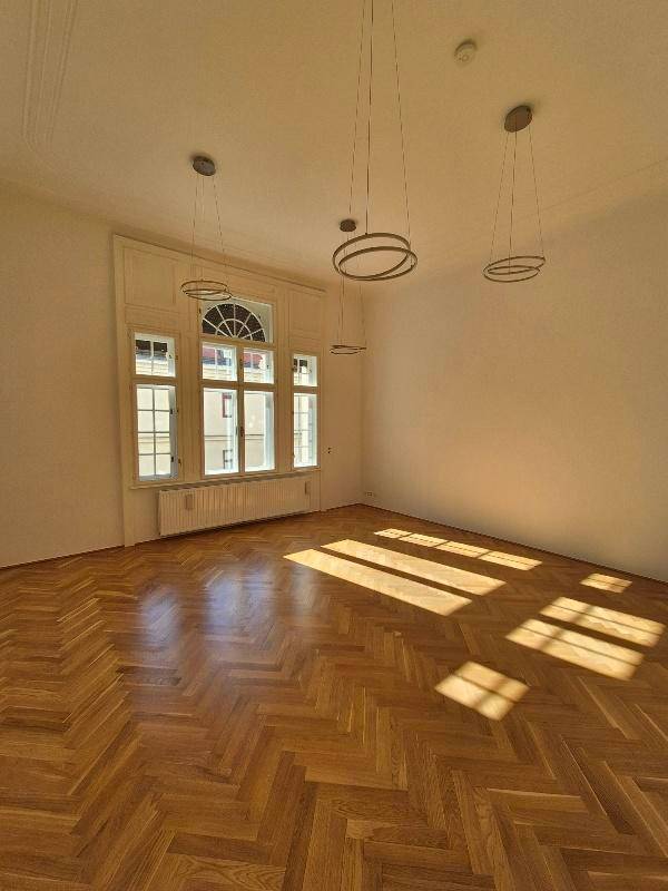 Lichtdurchflutetes Zimmer mit Fischgrätparkett, hohen Fenstern und modernen Hängelampen, sonnige Atmosphäre.