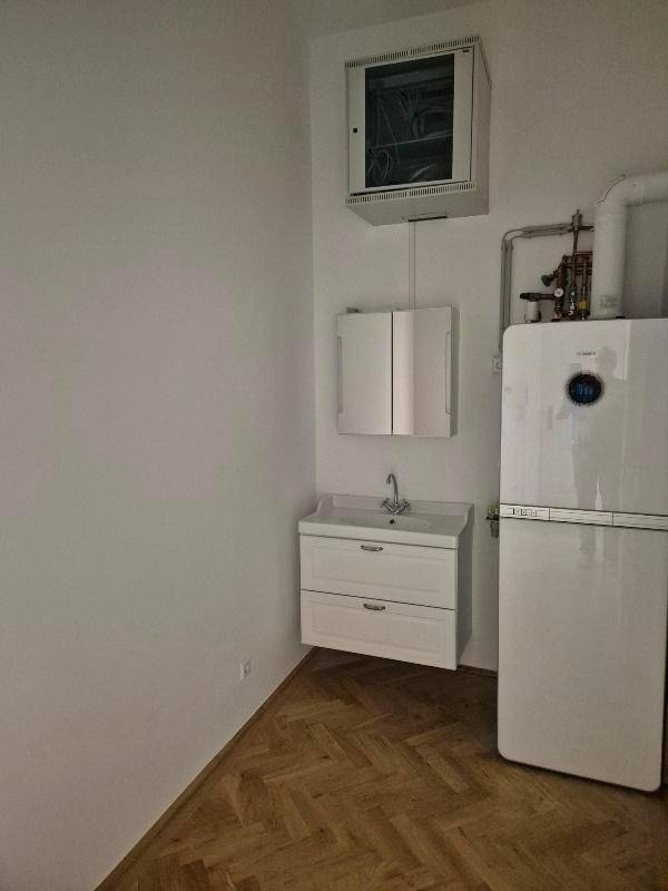 Praktischer Hauswirtschaftsraum mit Waschbecken, Kühlschrank und Elektroverteiler, ausgestattet mit Parkettboden.