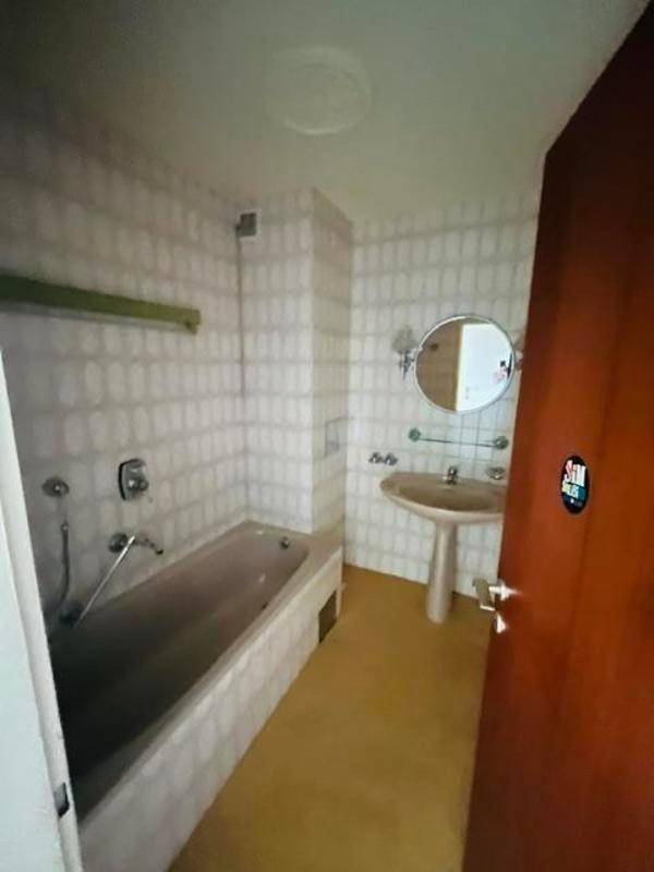 Badezimmer mit Badewanne, Waschbecken und hellen Fliesen im 80er-Jahre-Stil.