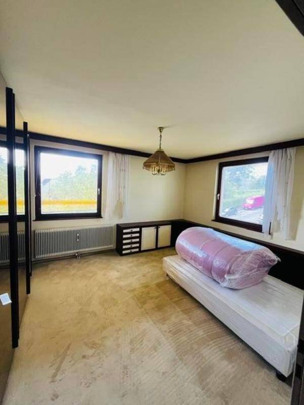 Geräumiges Schlafzimmer mit Teppichboden, großen Fenstern und einfacher Einrichtung.