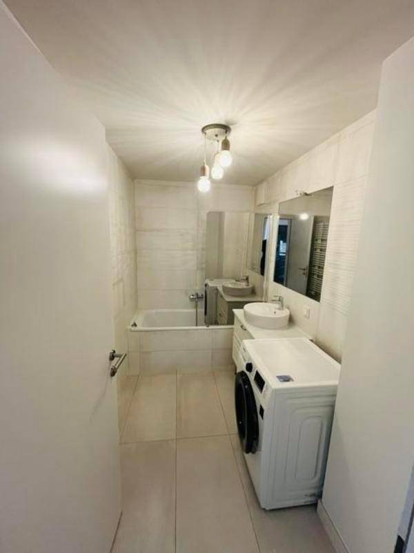 Modernes Badezimmer mit weißen Fliesen, Badewanne, Einzelwaschbecken und Waschmaschine.