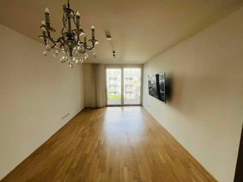 Geräumiges Wohnzimmer mit Parkettboden, Kronleuchter und Zugang zum sonnigen Balkon.