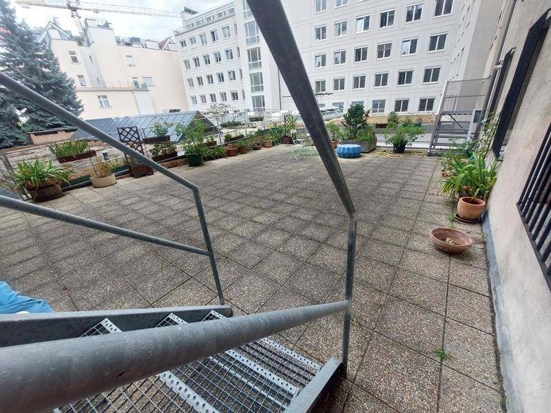 Große geflieste Gemeinschaftsterrasse mit vielen Pflanzen und Blick auf umliegende Gebäude.