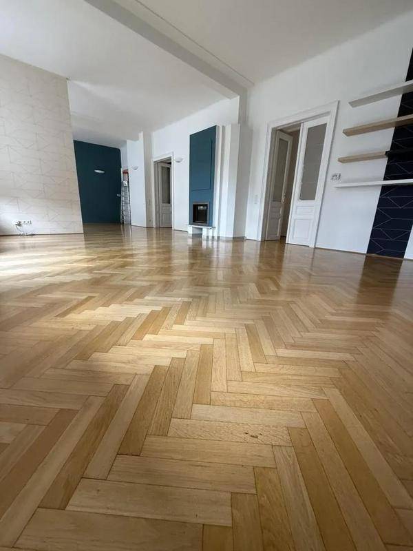 Geräumiges Wohnzimmer mit Fischgrätparkett, weißen Wänden und einem modernen Kamin.