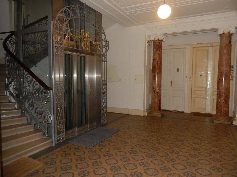 Prunkvoller Eingangsbereich eines Altbaus mit historischem Aufzug, Treppe und Marmorsäulen.
