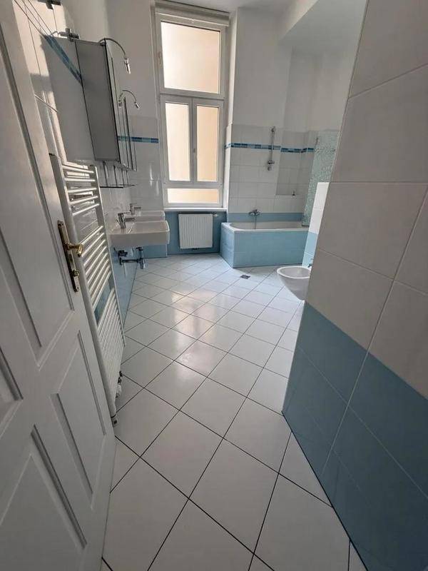 Geräumiges Badezimmer mit weißen und hellblauen Fliesen, Badewanne, Bidet und Fenster.