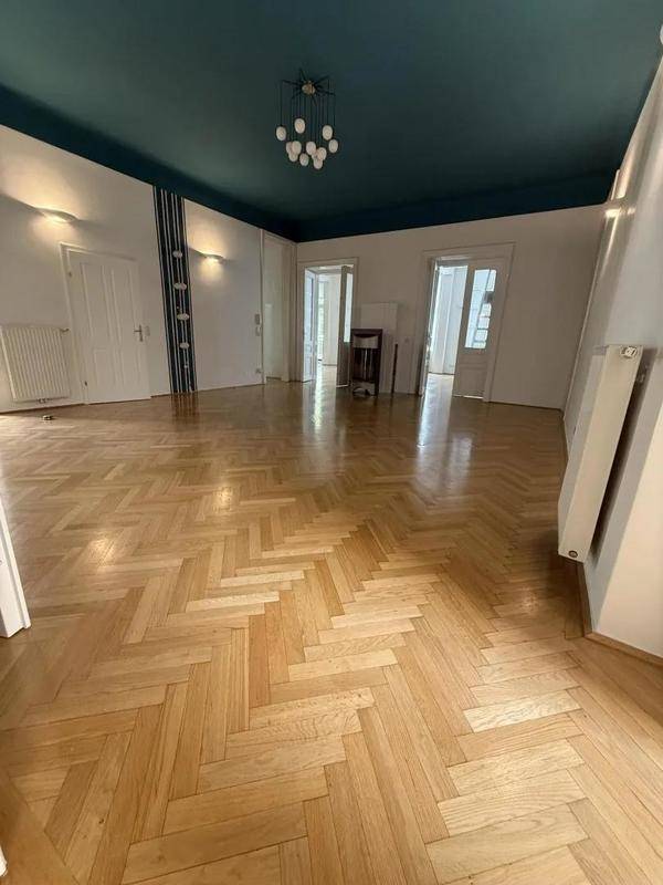 Großes Zimmer mit Fischgrätparkett, weißen Wänden und einer auffälligen dunkelblauen Decke.