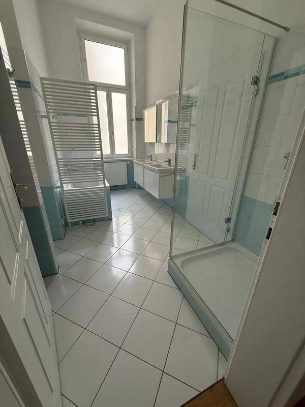 Helles Badezimmer mit weißen und hellblauen Fliesen, einer begehbaren Dusche und Doppelwaschbecken.