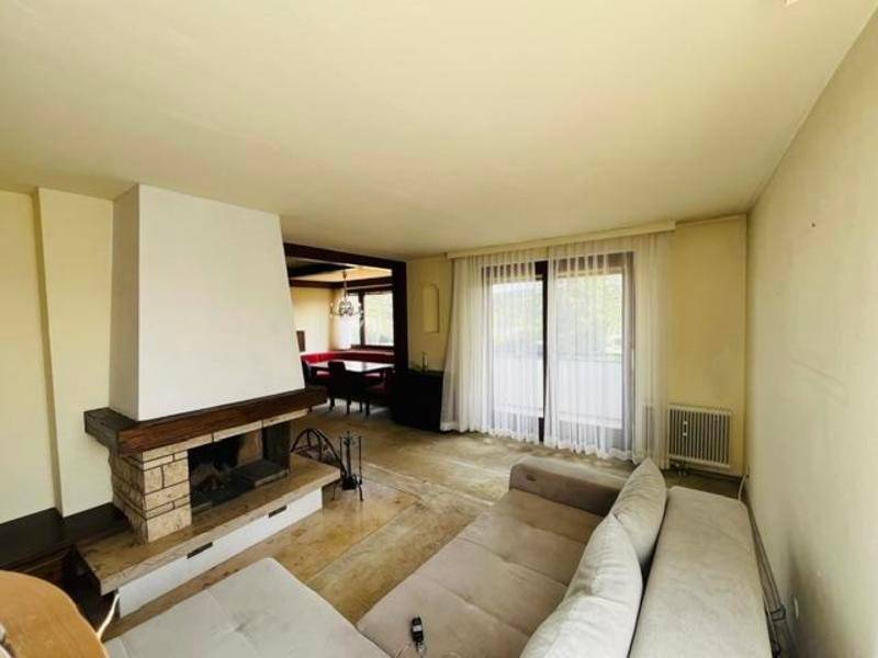 Geräumiges Wohnzimmer mit Kamin, großen Fenstern und Zugang zu einem Außenbereich.