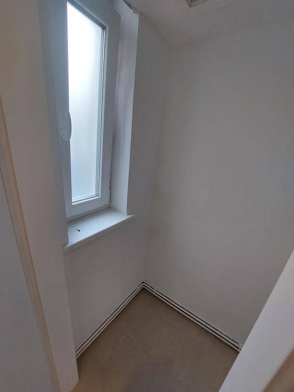 Kleiner Abstellraum mit Fenster, hellem Fliesenboden und weißen Wänden.