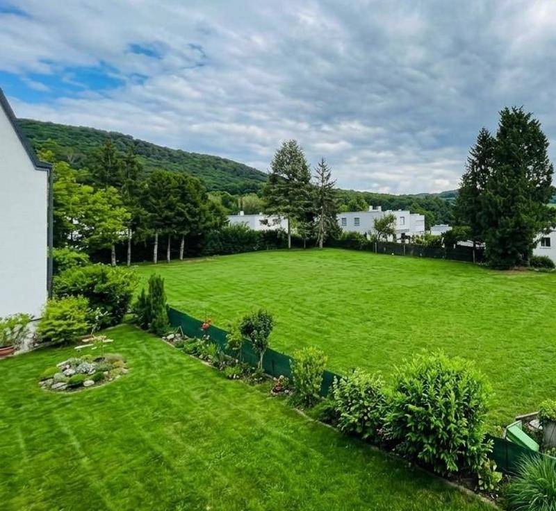 Großer, gepflegter Garten mit weitläufiger Rasenfläche und Blick auf bewaldete Hügel.