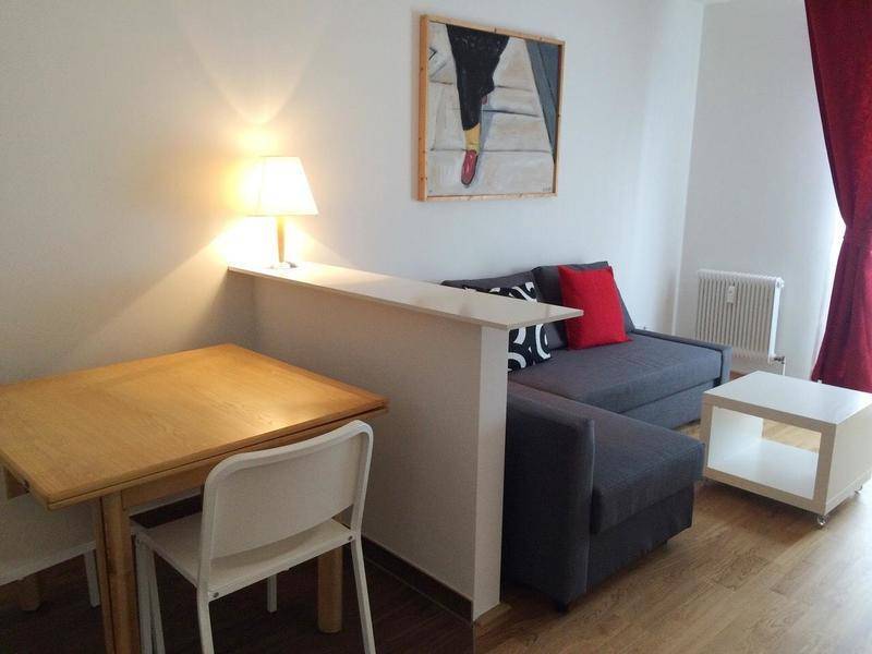 Gemütlicher Wohn- und Essbereich mit Sofa, Esstisch und Parkettboden, beleuchtet von einer Tischlampe.