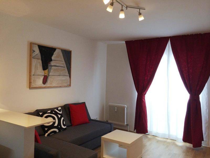 Heller Wohn- und Essbereich mit großen Fenstern, roten Vorhängen und einem modernen Sofa.