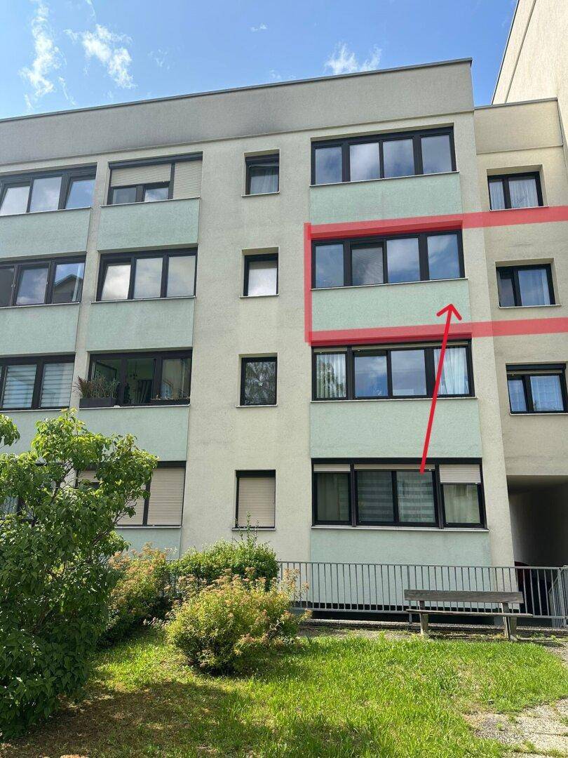 Mehrfamilienhaus mit moderner Fassade, vielen Fenstern und gepflegter Grünfläche im Vordergrund.