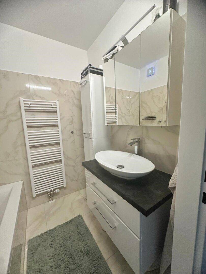 Modernes Badezimmer mit elegantem Aufsatzwaschbecken, Spiegelschrank und beheiztem Handtuchhalter.