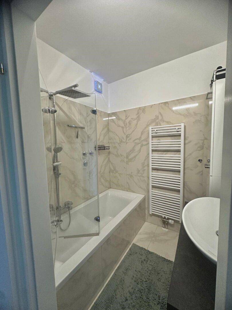 Helles Badezimmer mit Badewanne, integrierter Dusche und modernen Fliesen an Wänden und Boden.