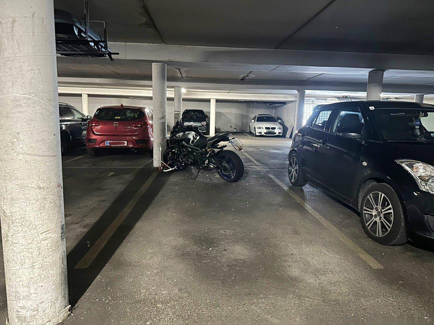 Tiefgarage mit mehreren Stellplätzen und geparkten Fahrzeugen, inklusive Motorrad.
