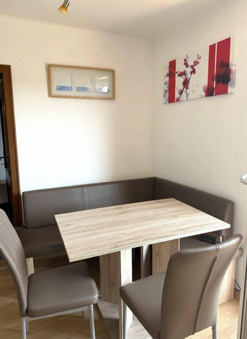 Heller Essbereich mit Eckbank und modernem Holztisch, dekoriert mit einem abstrakten Wandbild.